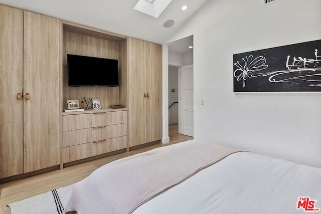 bedroom featuring vaulted ceiling with skylight and light hardwood / wood-style floors