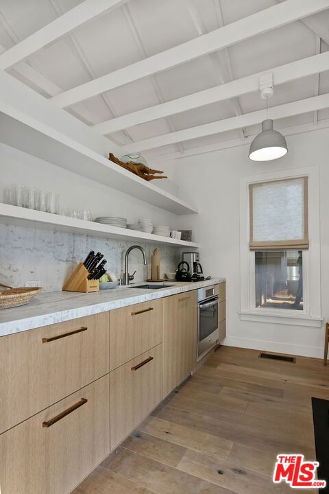 kitchen featuring sink, stainless steel oven, light brown cabinets, pendant lighting, and light hardwood / wood-style floors