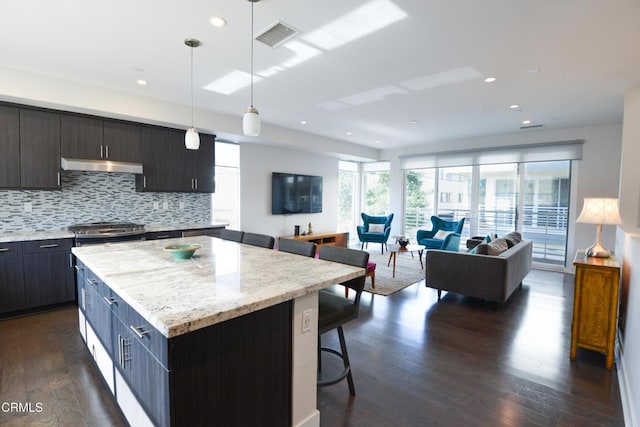 kitchen featuring hanging light fixtures, a kitchen breakfast bar, dark hardwood / wood-style floors, a center island, and decorative backsplash