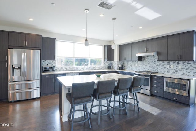 kitchen with pendant lighting, a breakfast bar, stainless steel appliances, a center island, and dark hardwood / wood-style flooring