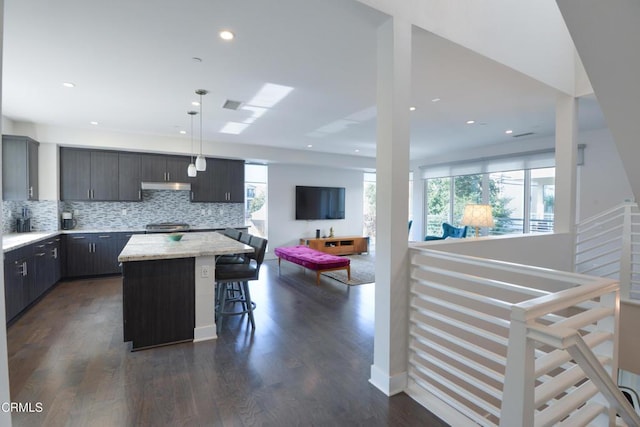 kitchen featuring a breakfast bar, decorative backsplash, hanging light fixtures, a center island, and dark wood-type flooring