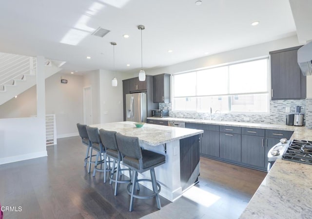 kitchen featuring appliances with stainless steel finishes, hanging light fixtures, a center island, light stone countertops, and a kitchen bar