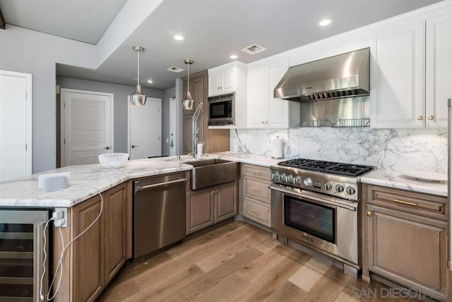 kitchen featuring wall chimney range hood, white cabinetry, stainless steel appliances, tasteful backsplash, and beverage cooler