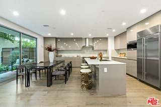 kitchen featuring gray cabinetry, a kitchen island with sink, built in fridge, wall chimney exhaust hood, and light wood-type flooring