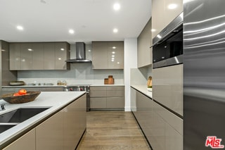 kitchen with gray cabinetry, light hardwood / wood-style floors, wall chimney exhaust hood, and appliances with stainless steel finishes