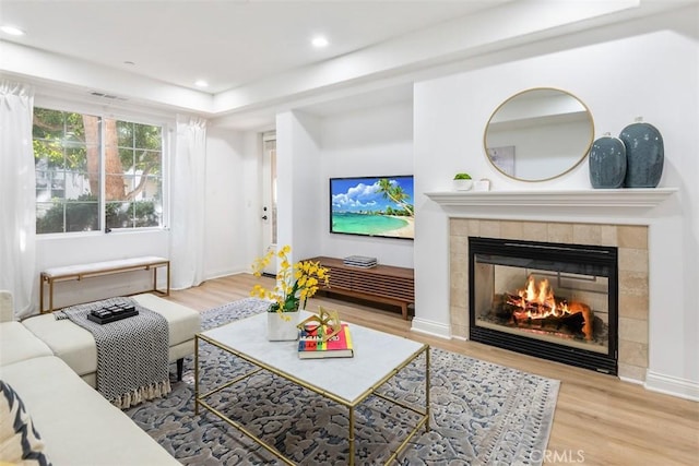 living room with a tiled fireplace and light hardwood / wood-style flooring