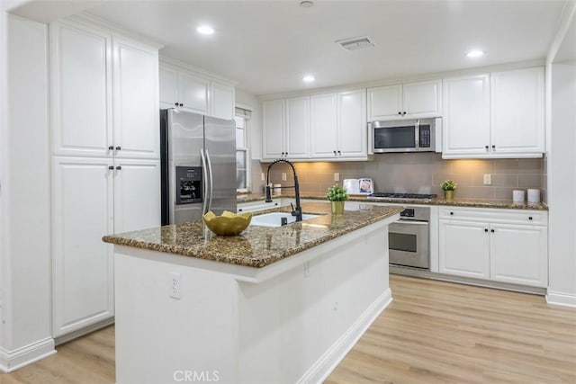 kitchen with white cabinetry, an island with sink, sink, dark stone counters, and stainless steel appliances