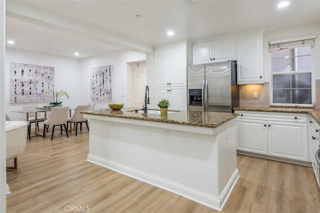 kitchen with sink, dark stone countertops, white cabinets, stainless steel fridge, and a kitchen island with sink