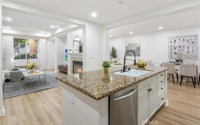 kitchen featuring sink, white cabinetry, a center island with sink, light hardwood / wood-style flooring, and stainless steel dishwasher