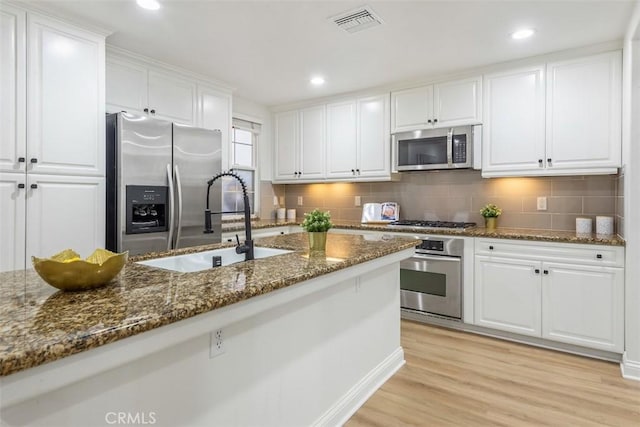 kitchen with sink, light hardwood / wood-style flooring, appliances with stainless steel finishes, white cabinetry, and dark stone counters