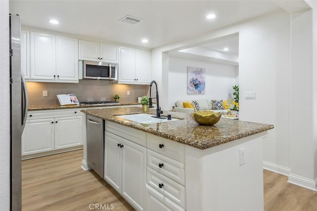 kitchen with sink, white cabinetry, dark stone countertops, appliances with stainless steel finishes, and an island with sink