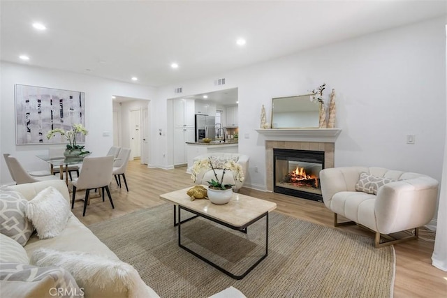 living room featuring a tiled fireplace and light hardwood / wood-style floors