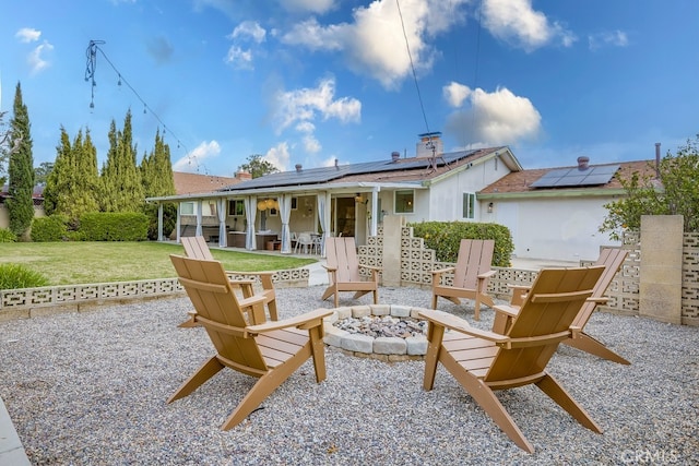 rear view of house featuring a yard, a patio, solar panels, and an outdoor fire pit