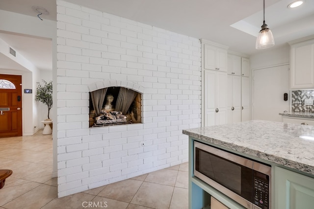 kitchen featuring light tile patterned floors, light stone countertops, decorative backsplash, white cabinets, and decorative light fixtures