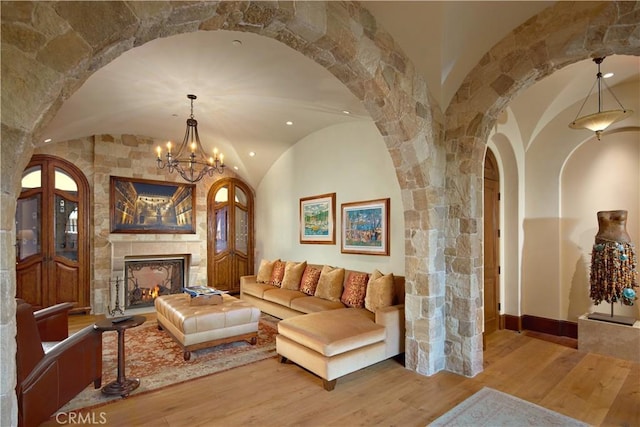 living room with light hardwood / wood-style flooring, brick ceiling, a fireplace, vaulted ceiling, and a chandelier