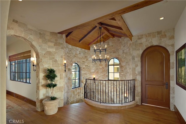 corridor with an inviting chandelier, vaulted ceiling with beams, and light wood-type flooring