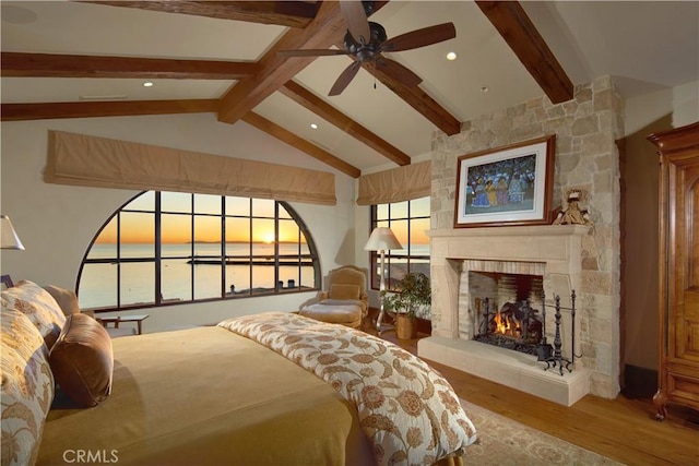 bedroom with hardwood / wood-style flooring, a stone fireplace, vaulted ceiling with beams, and ceiling fan