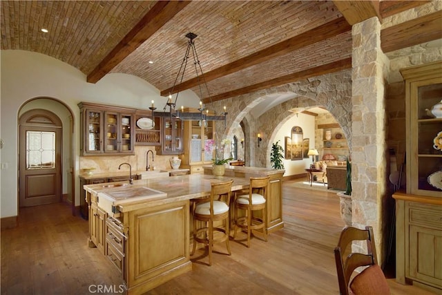 interior space with lofted ceiling, brick ceiling, hanging light fixtures, light hardwood / wood-style floors, and an island with sink