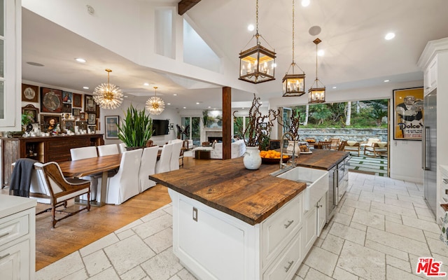 kitchen with sink, butcher block countertops, white cabinetry, hanging light fixtures, and a kitchen island with sink