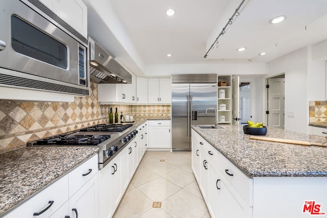 kitchen featuring range hood, white cabinetry, backsplash, a center island, and built in appliances