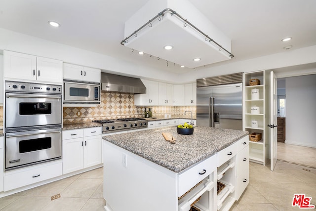 kitchen with white cabinets, built in appliances, a kitchen island, and wall chimney range hood