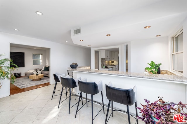 kitchen with a breakfast bar, light tile patterned floors, light stone counters, and kitchen peninsula