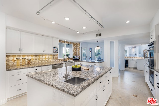 kitchen featuring appliances with stainless steel finishes, white cabinetry, an island with sink, sink, and beverage cooler