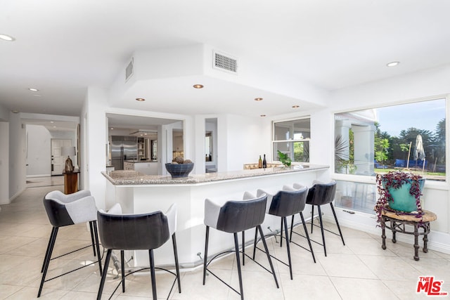 kitchen featuring light stone counters, a kitchen breakfast bar, stainless steel built in fridge, and light tile patterned floors