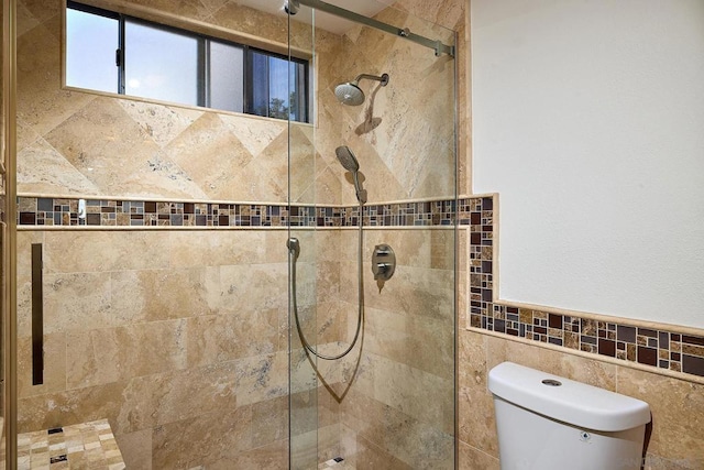 bathroom featuring toilet, a shower with door, and tile walls