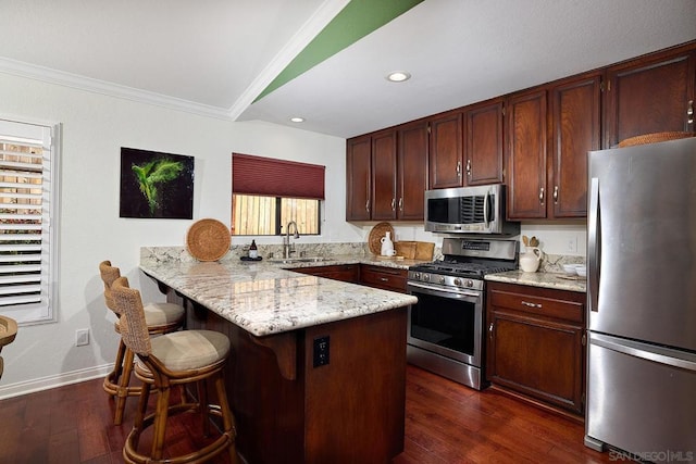 kitchen with appliances with stainless steel finishes, sink, a kitchen breakfast bar, kitchen peninsula, and crown molding