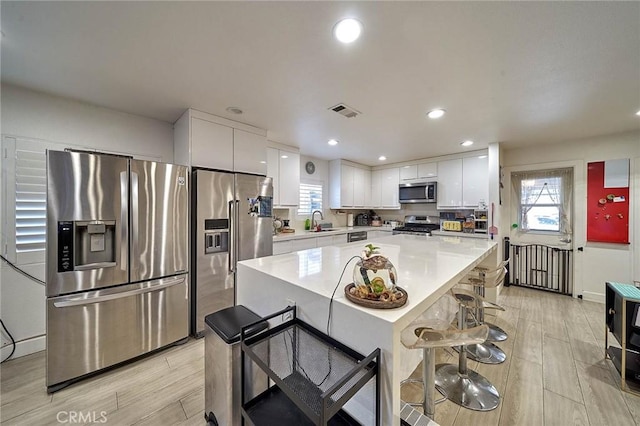 kitchen featuring appliances with stainless steel finishes, white cabinetry, sink, a kitchen bar, and a center island