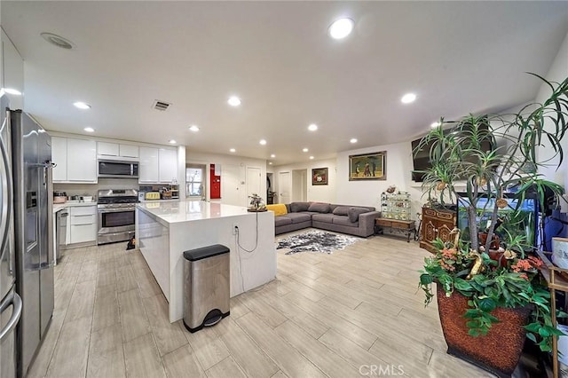 kitchen featuring stainless steel appliances, white cabinetry, a center island, and light wood-type flooring