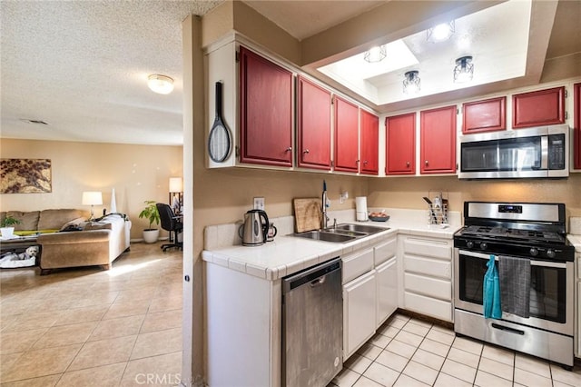 kitchen with appliances with stainless steel finishes, sink, light tile patterned floors, and a textured ceiling