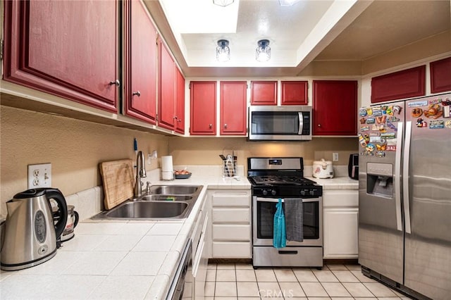 kitchen with appliances with stainless steel finishes, sink, light tile patterned floors, and tile counters