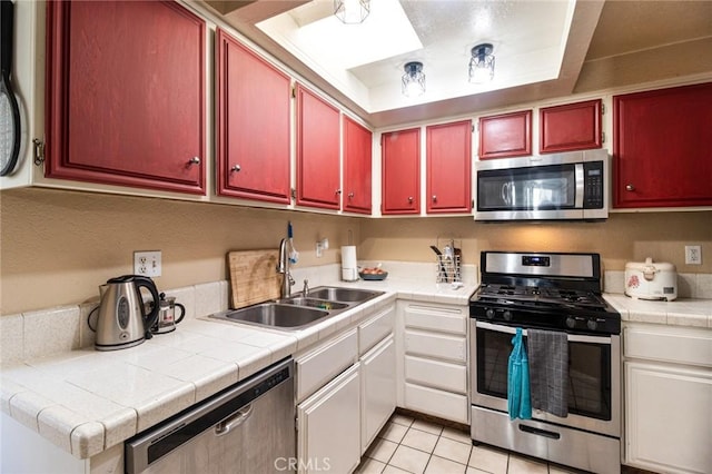 kitchen with sink, tile counters, light tile patterned flooring, and appliances with stainless steel finishes