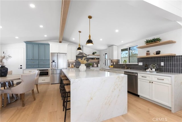 kitchen featuring white cabinetry, decorative light fixtures, a center island, stainless steel appliances, and light stone countertops