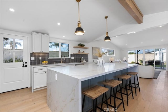 kitchen featuring decorative light fixtures, vaulted ceiling with beams, white cabinets, light stone countertops, and a spacious island