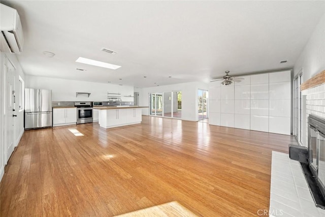 unfurnished living room with light hardwood / wood-style floors, a fireplace, a wall unit AC, and a skylight