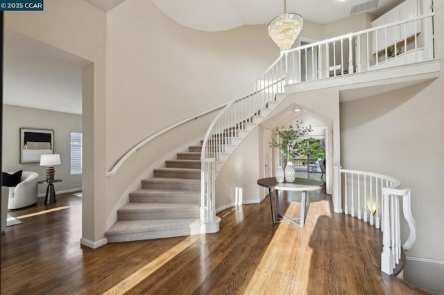 stairs with an inviting chandelier, a towering ceiling, and hardwood / wood-style floors