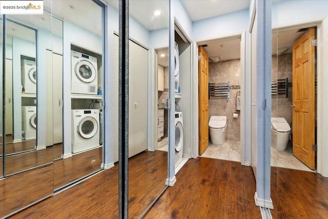 clothes washing area with stacked washer and clothes dryer and wood-type flooring