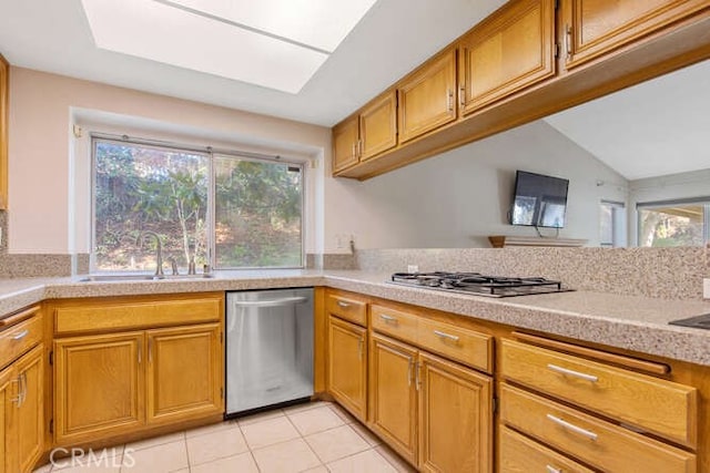 kitchen featuring stainless steel appliances, lofted ceiling with skylight, sink, and light tile patterned floors