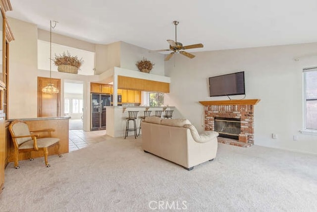 living room featuring light carpet, a brick fireplace, a towering ceiling, and ceiling fan