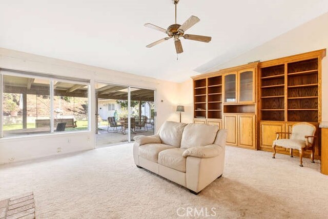 carpeted living room with ceiling fan and vaulted ceiling