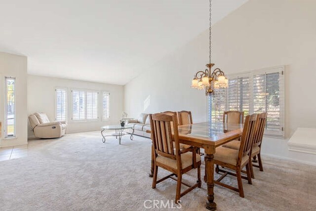 dining space with light colored carpet, plenty of natural light, lofted ceiling, and a notable chandelier