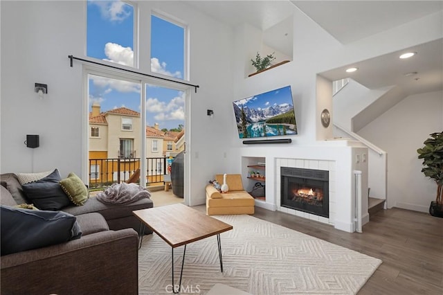 living room featuring hardwood / wood-style flooring, a towering ceiling, and a tile fireplace