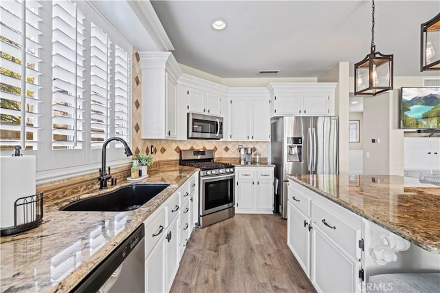 kitchen featuring appliances with stainless steel finishes, sink, white cabinets, and decorative light fixtures