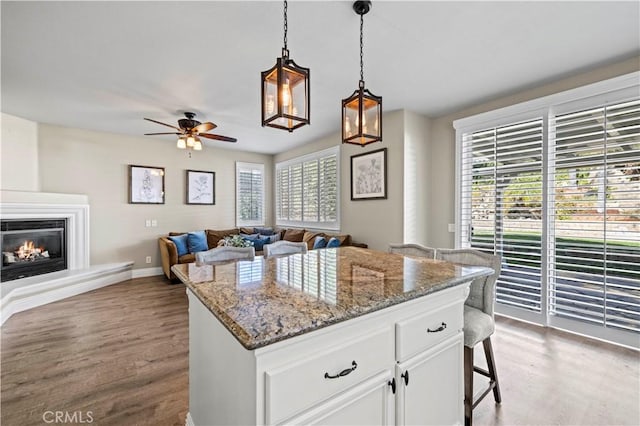 kitchen featuring stone countertops, a breakfast bar, white cabinetry, hanging light fixtures, and a center island