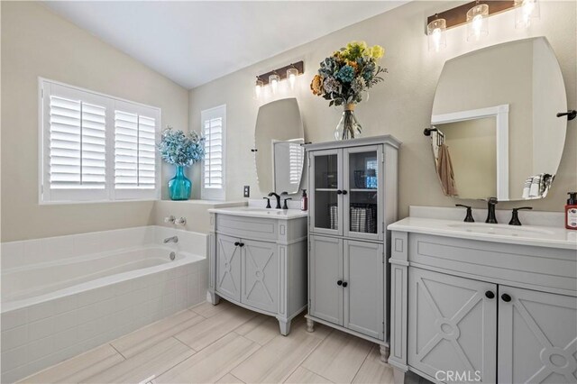 bathroom with vanity, a relaxing tiled tub, and lofted ceiling