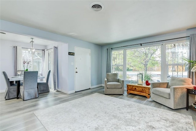 living room with a wealth of natural light, an inviting chandelier, and light hardwood / wood-style flooring