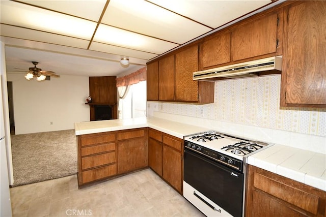 kitchen featuring white gas range oven, ceiling fan, tile counters, light colored carpet, and kitchen peninsula